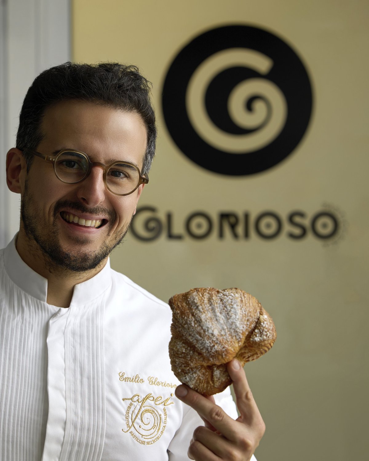 Emilio Glorioso sorride con in mano uno sfogliato, davanti all'insegna Glorioso