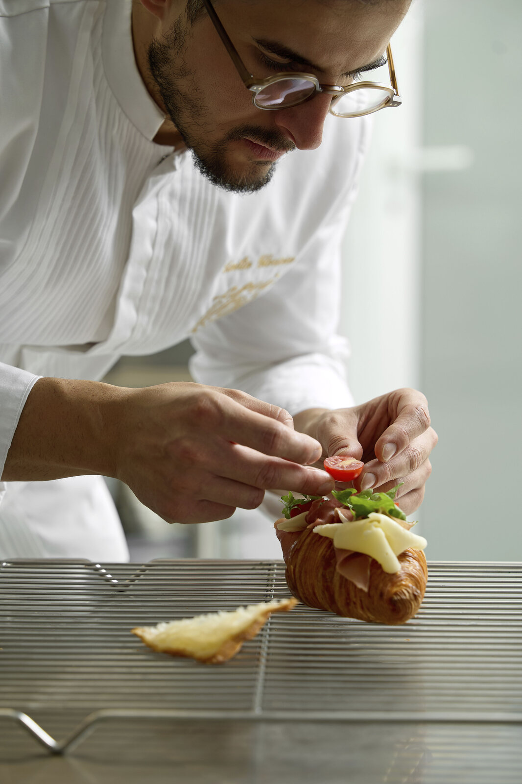 Il pasticcere farcisce un croissant salato con prosciutto, formaggio, rucola e pomodorino