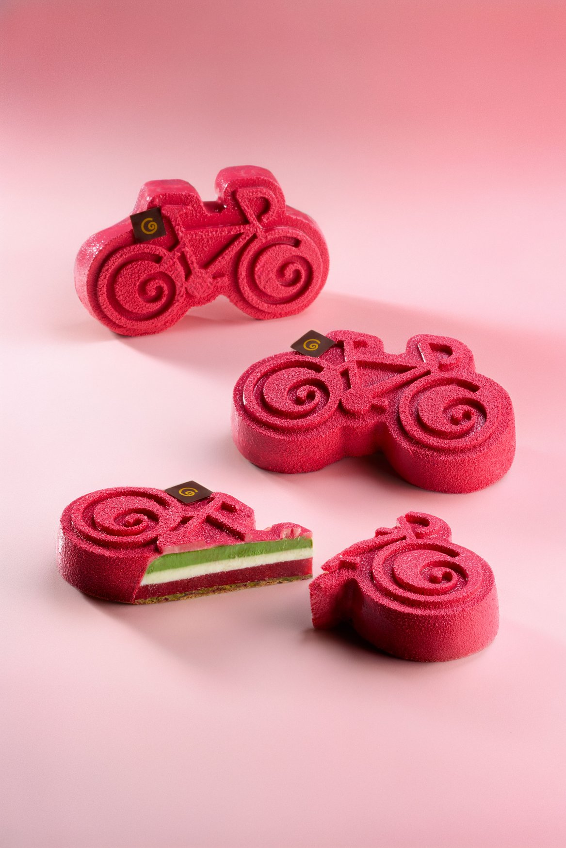Dolce scolpito a forma di bicicletta, con glassa rosa ai frutti rossi